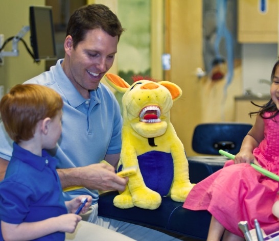 Pediatric dentist using stuffed animal to show kids how to brush teeth