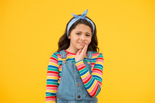 Girl in striped shirt holding hand to jaw in pain with yellow background