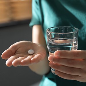 Person with a glass of water and pill in their hand