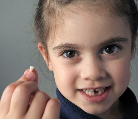 Young child holding up a tooth after extraction and showing gap in smile